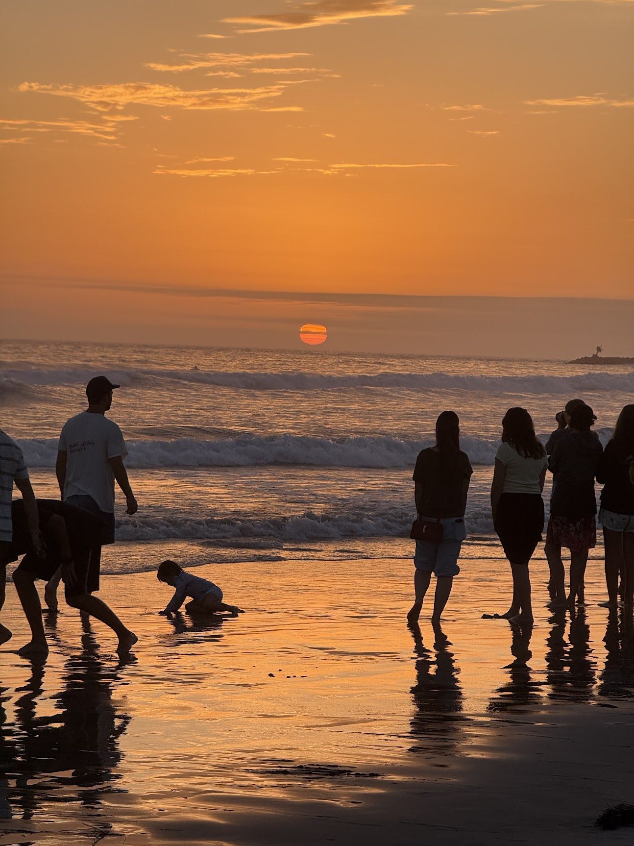 Sunset over the Pacific Ocean in Oceanside, California, with people standing at the water’s edge.